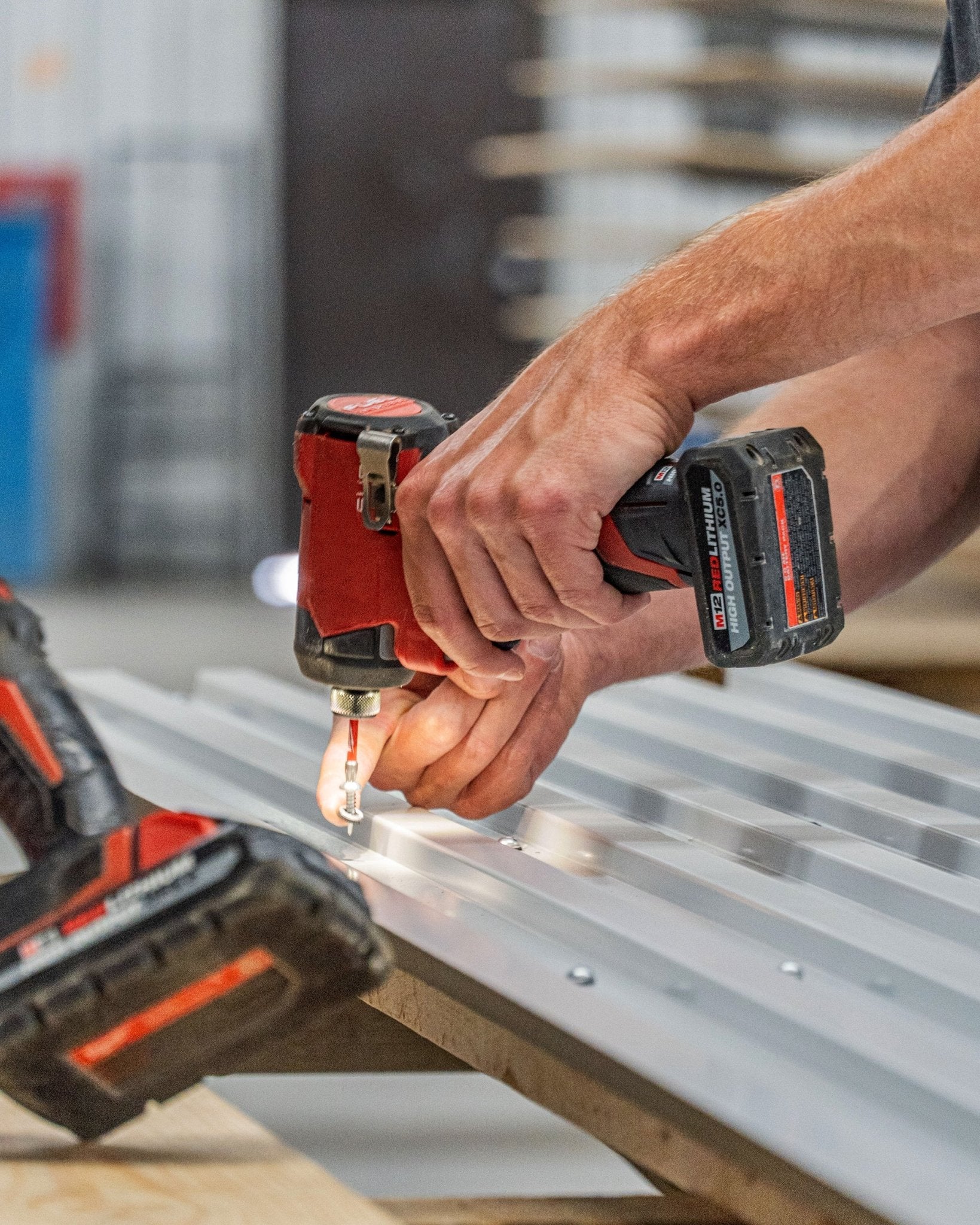 En person monterar WoodUpp Backside-skruvar 4,8x19 med Ø10 bricka TX20 (black) för att fästa Akustikpanel i plåt på en arbetsbänk.